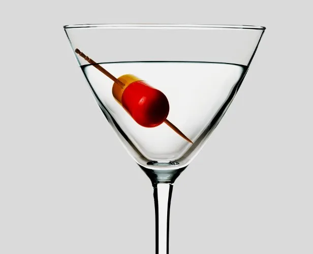 Image of martini-style cocktail with a medicine capsule on the toothpick on a grey background.