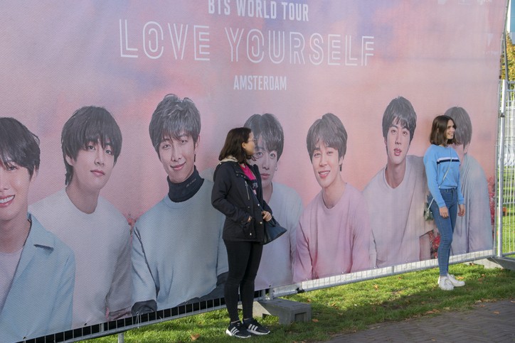 Two Women Posing In Front Of A Billboard For The BTS Concert in Amsterdam