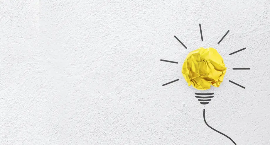 A yellow paper crumpled ball on a wall with black lines drawn out and down, representing an idea lightbulb.